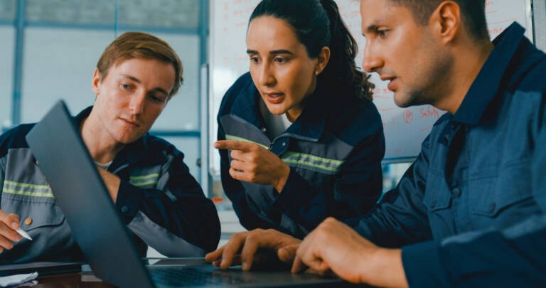 manufacturing engineers collaborating around a laptop to review production data and prepare systems, processes, and teams for successful AI implementation