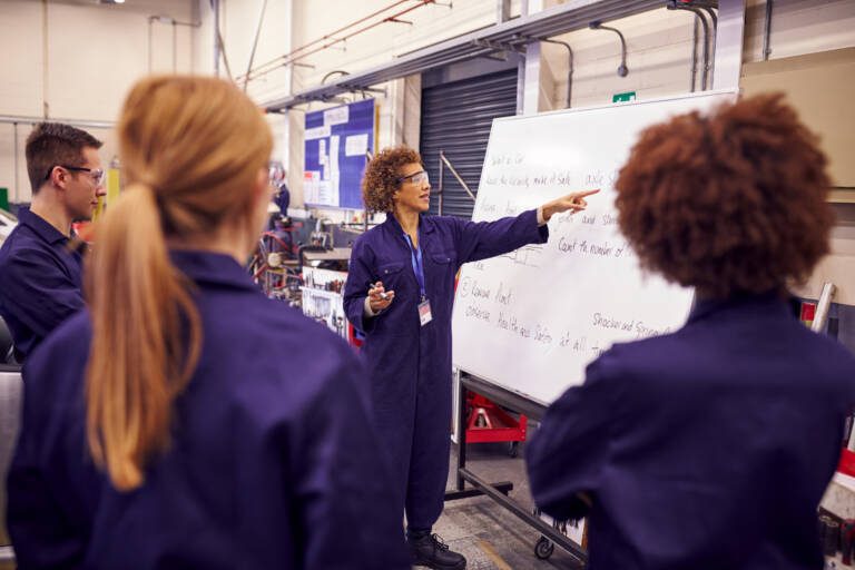 manufacturing instructor leading AI readiness training with plant employees gathered around a whiteboard during an industrial workforce development session