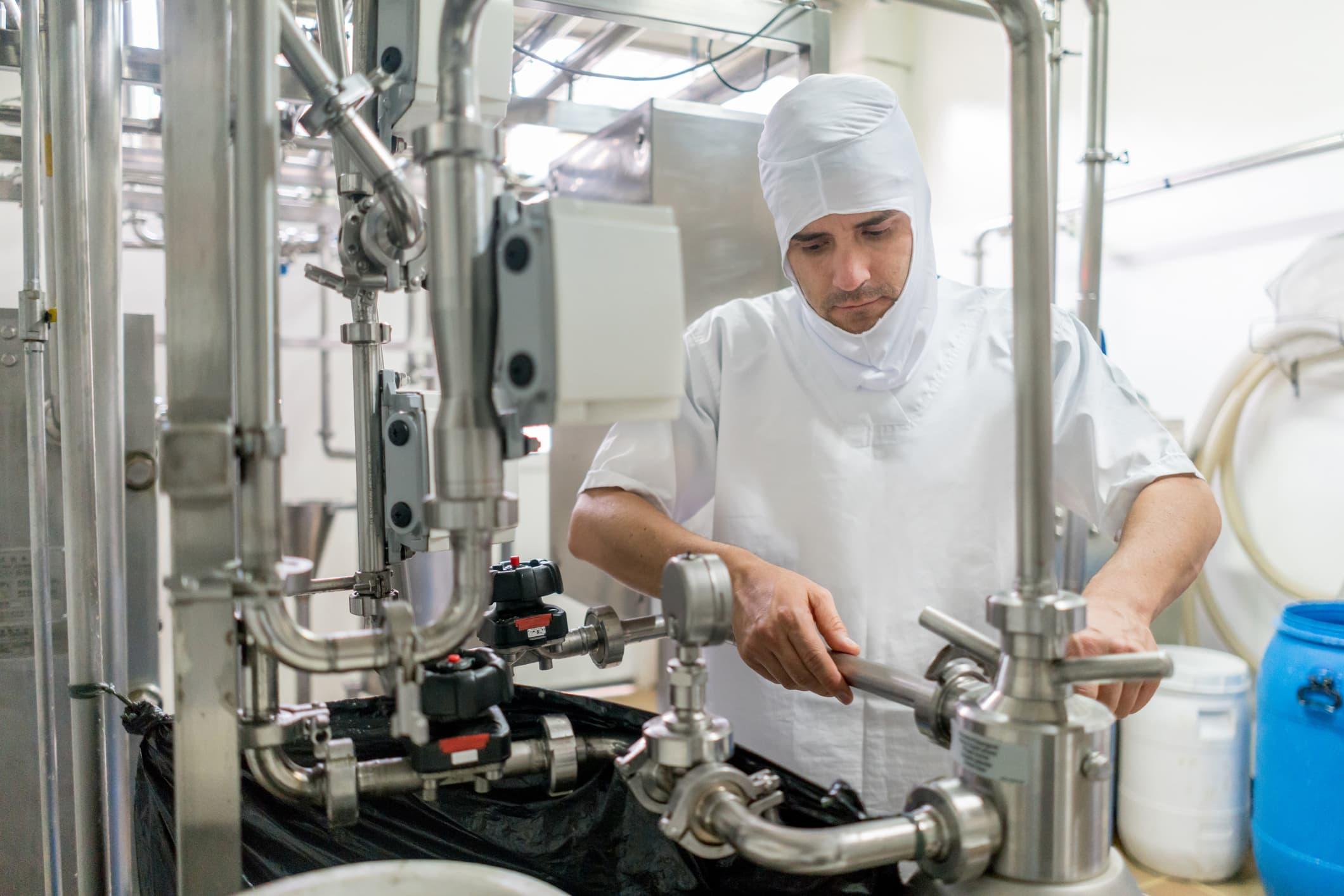 operator in sanitary protective gear managing stainless steel processing equipment in a modern food production facility