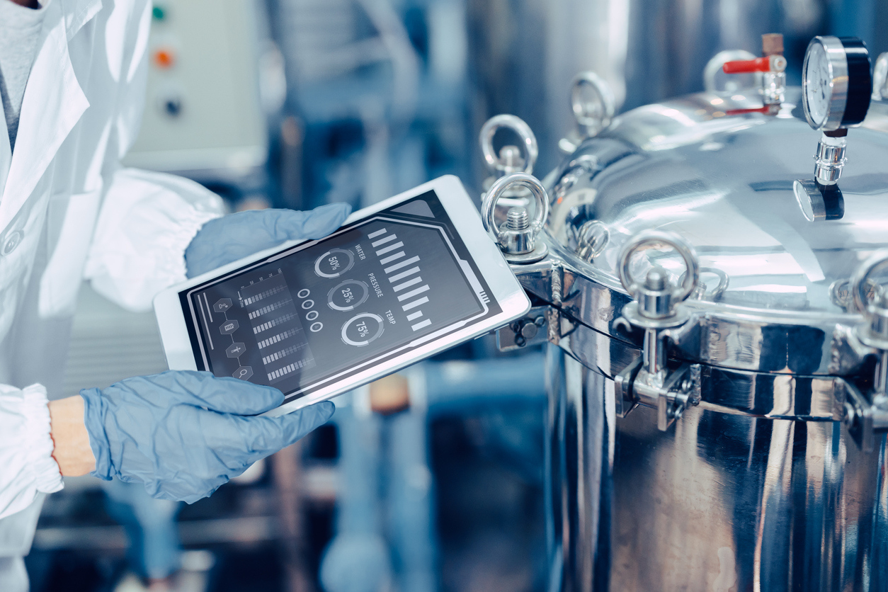 technician using a tablet to monitor manufacturing equipment and production data in a digitally connected industrial facility
