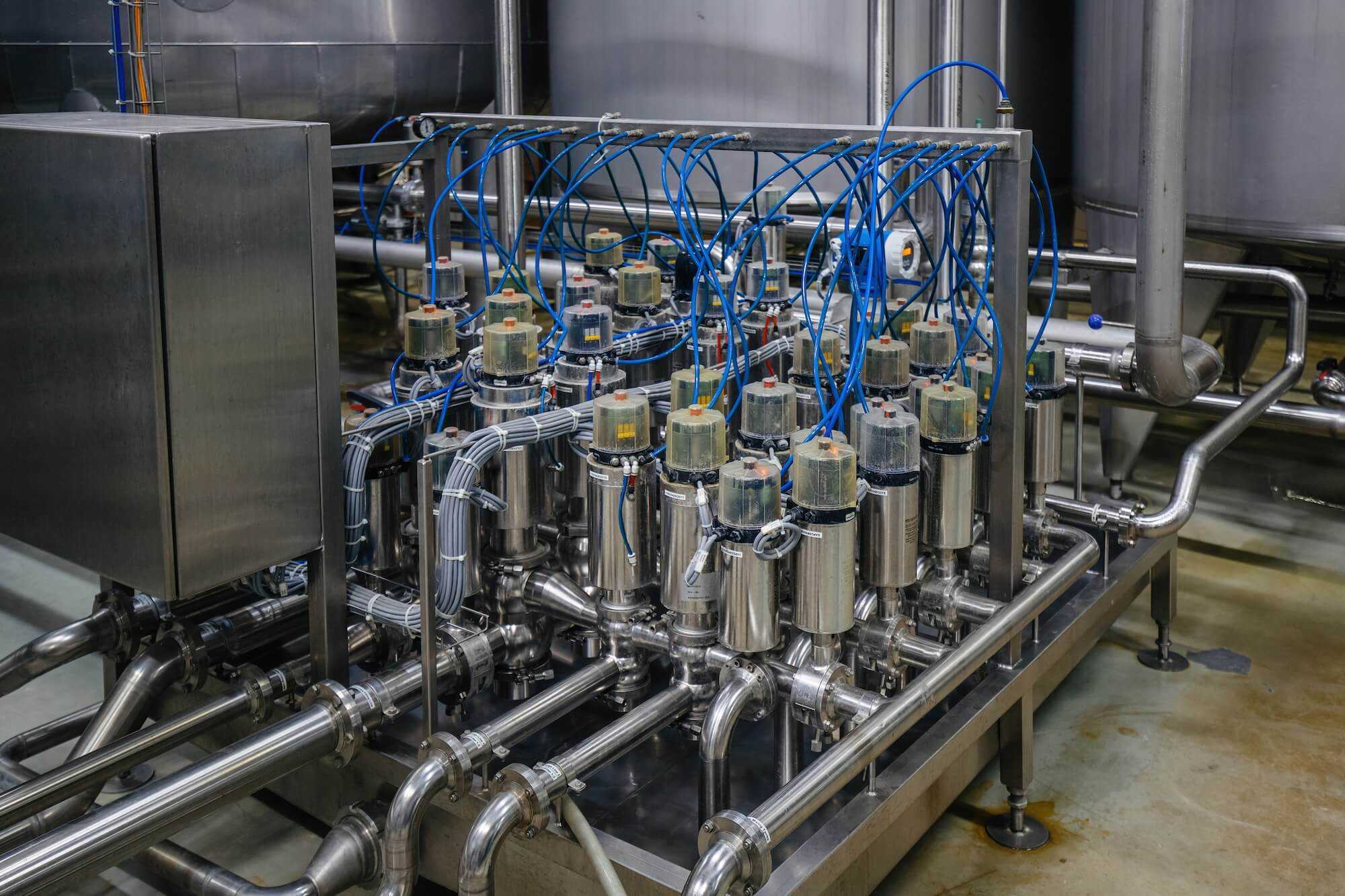 a dense matrix of stainless‑steel mixproof separation valves connected by piping and blue control lines inside a sanitary processing facility