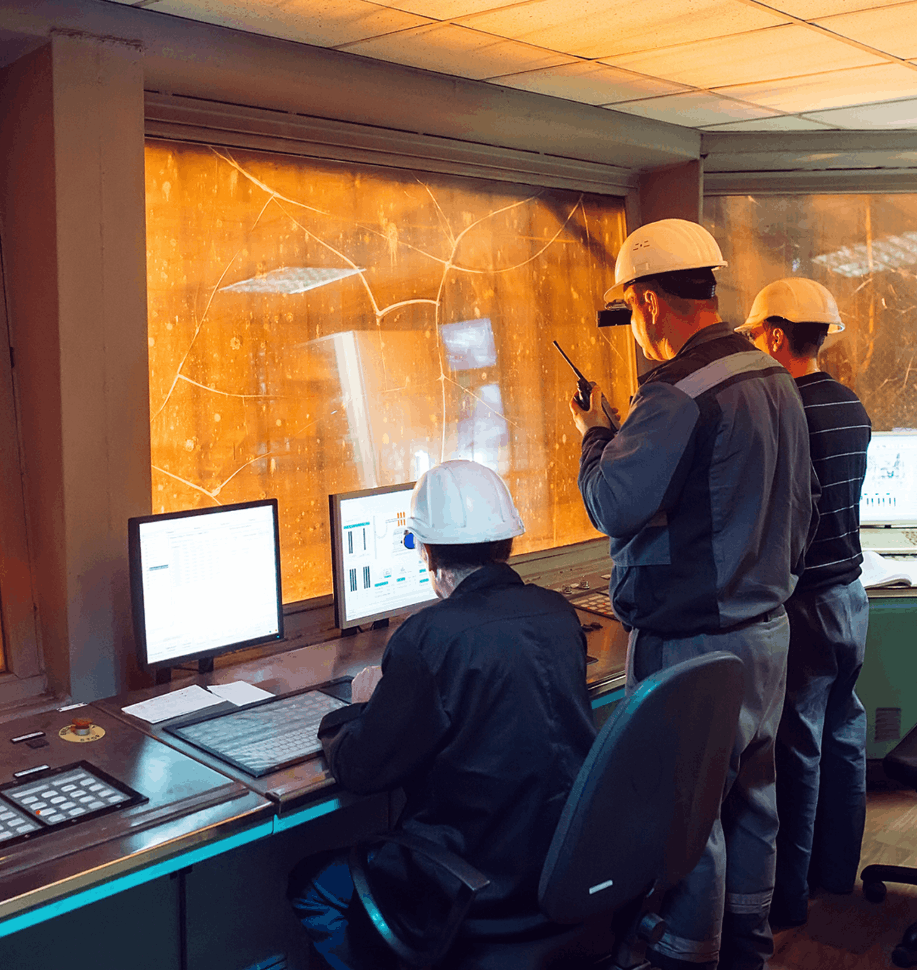 control room operators monitoring live steel production data with multiple screens and high‑heat processes visible through the windows illustrating real time analysis used to predict faults and maintain stable operations